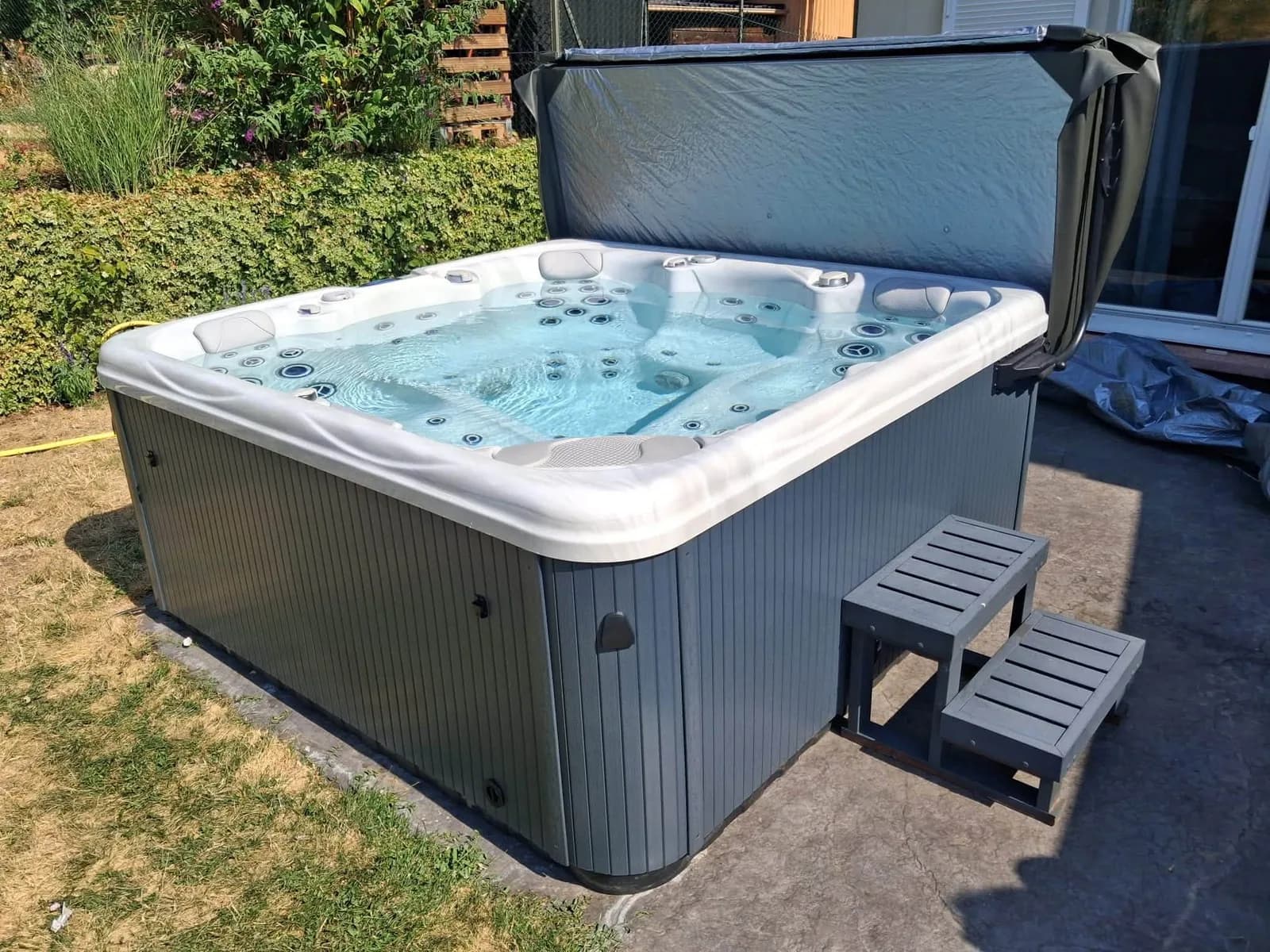 Installation d'un spa Athena à Niedermorschwihr, sur une dalle devant un massif de graminées
