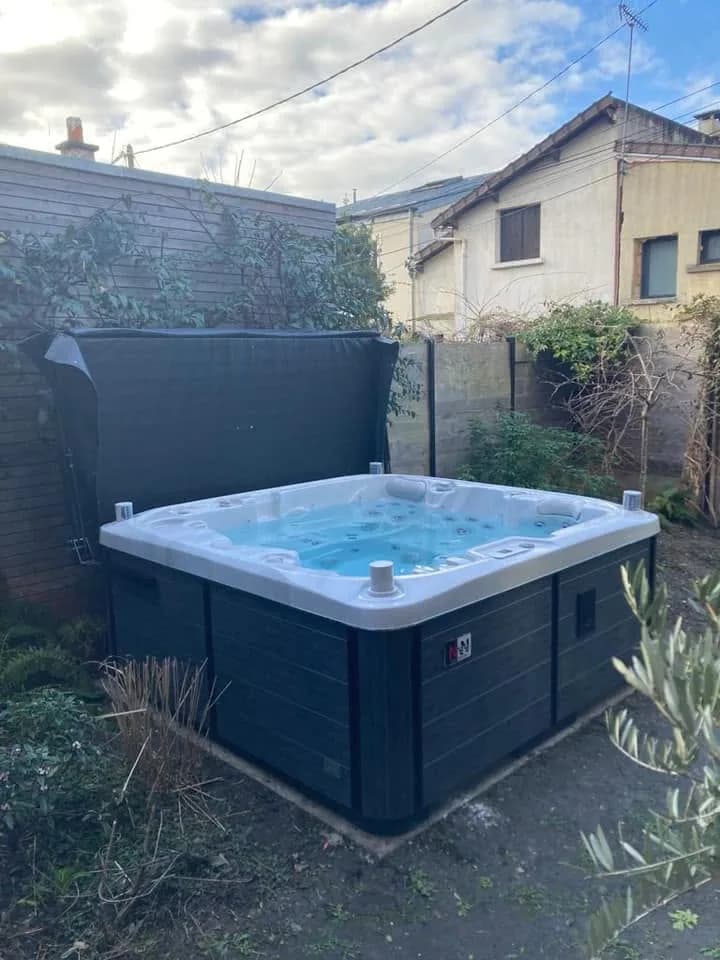 Installation d'un spa Bjørgan Full option, dans un jardin devant une palissade grise