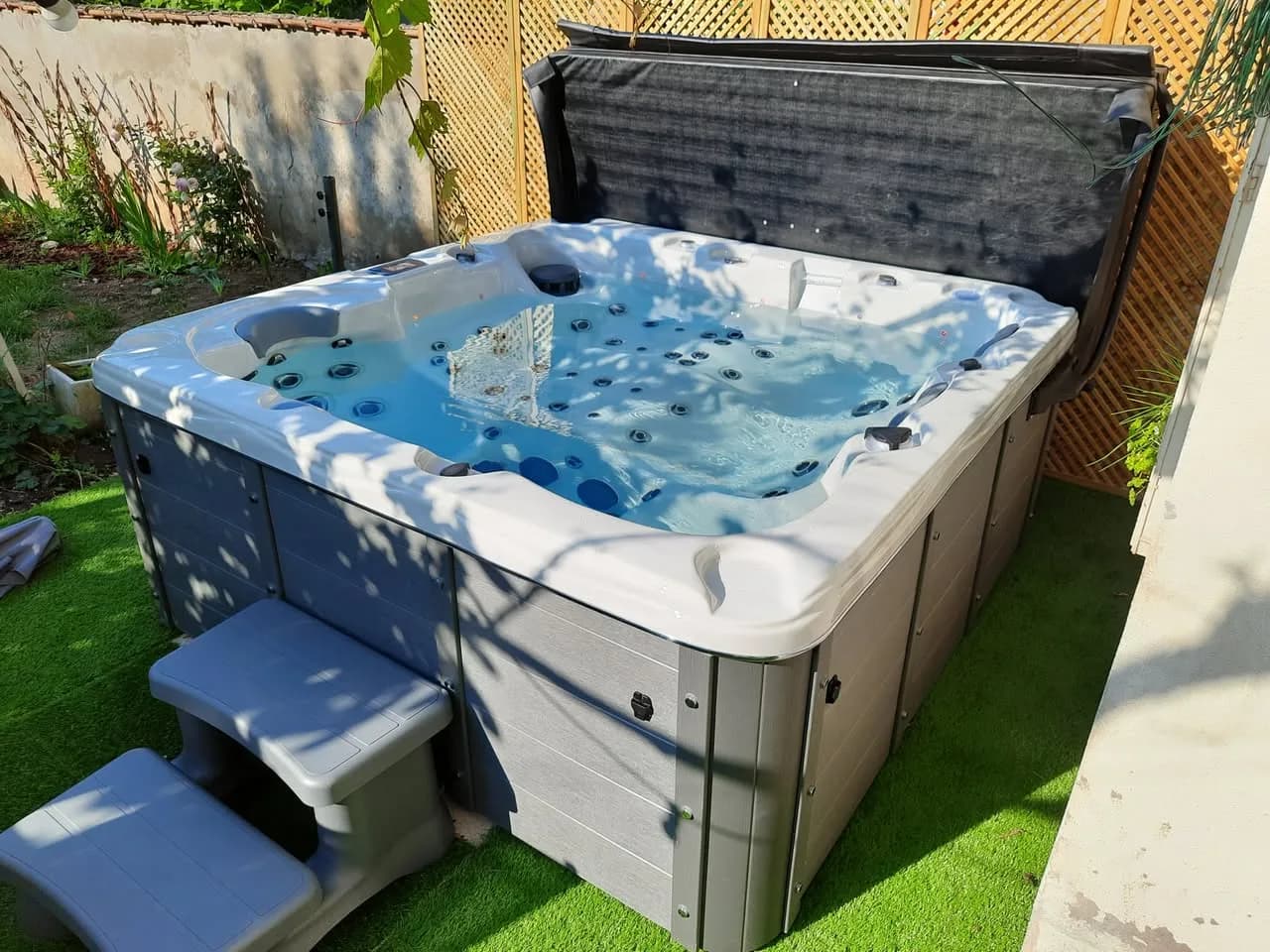 Installation d'un spa Burlington à Nancy, sur un gazon synthétique devant un treillis en bois