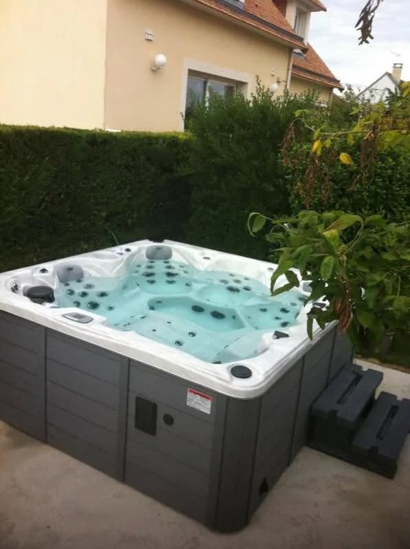 Installation d'un spa Cambridge Duel Full option dans le Calvados, devant une haie, marchepied