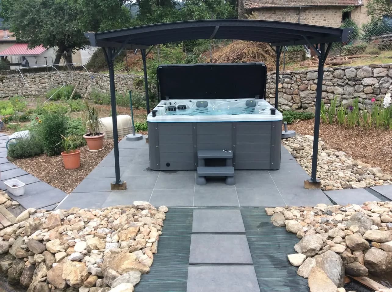 Installation d'un spa Cambridge Duel Full option à Grandrif, sous une pergola, jardin bordé de galets
