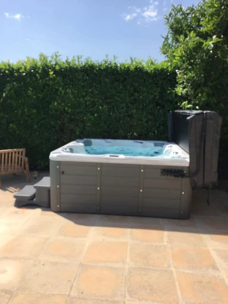 Installation d'un spa Cambridge Duel à Viré, sur une terrasse en terre cuite devant une haie
