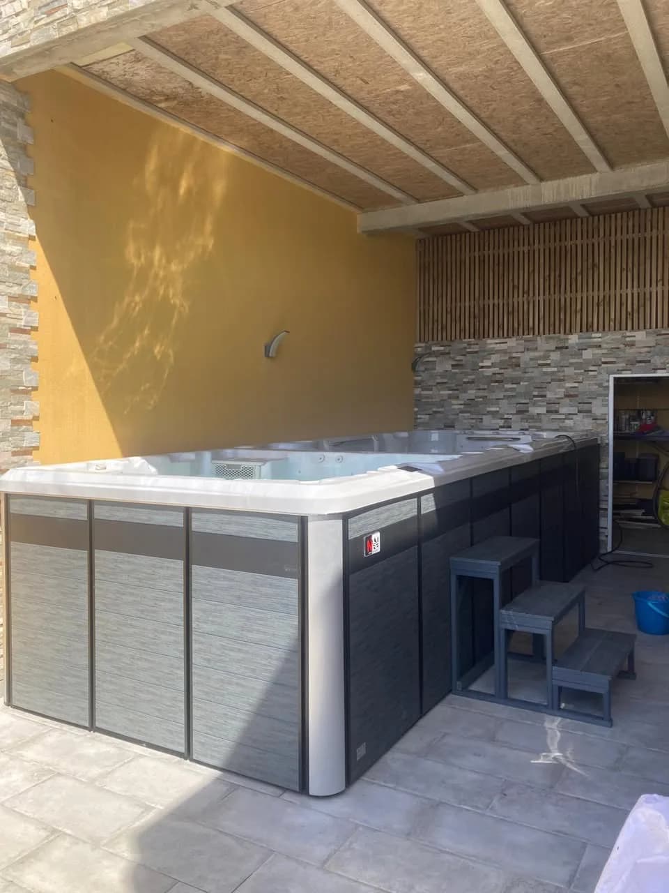 Installation d'un spa de nage Øslø 600, sous un préau contre un mur en pierre