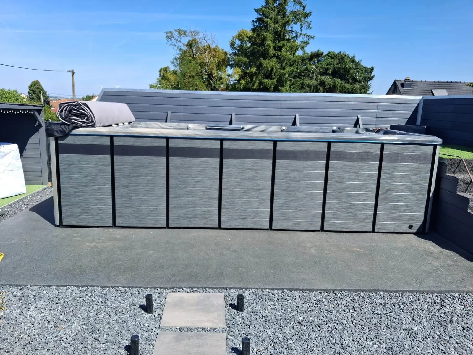 Installation d'un spa de nage Sløvika à Insming, sur une dalle anthracite bordée de gravier, enrouleur de couverture