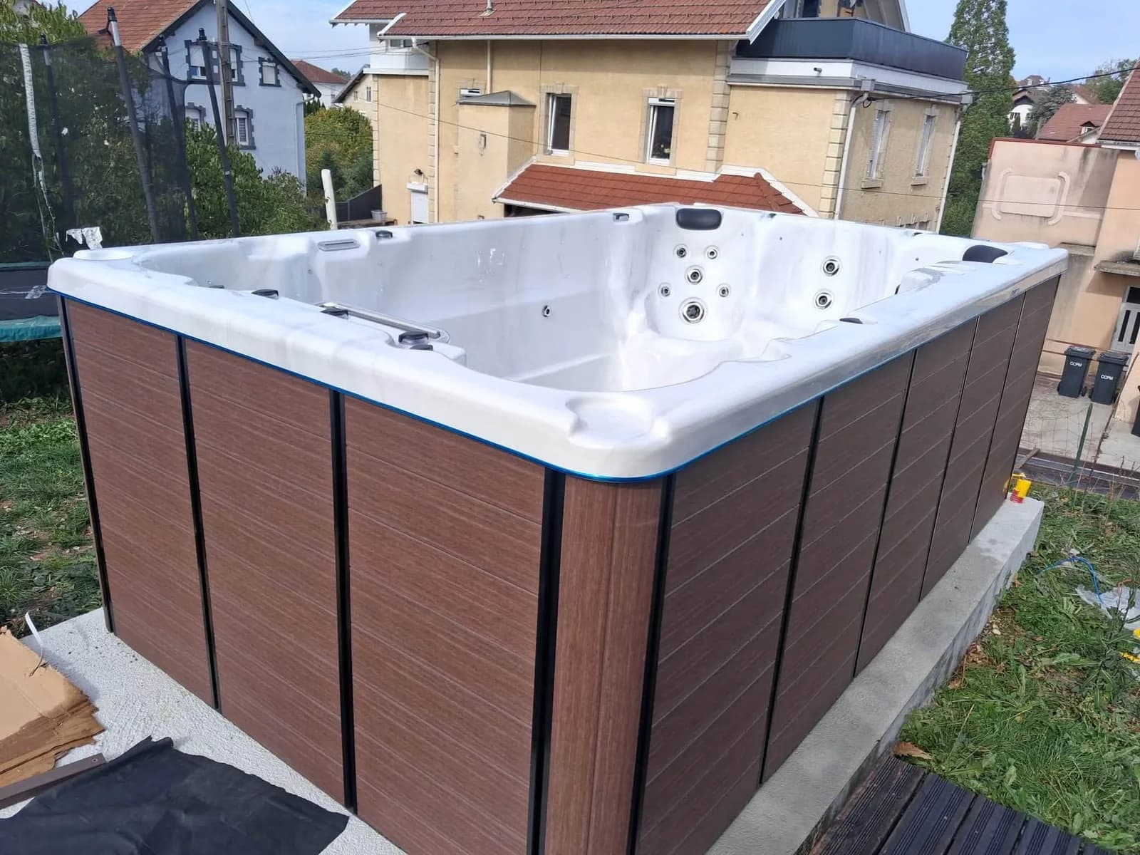 Installation d'un spa de nage Waterloo 390 à Charquemont, tablier brun, sur une dalle prolongée d'une terrasse en bois