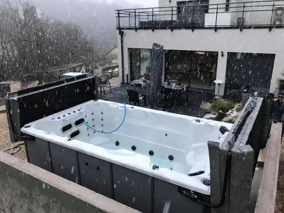 Installation d'un spa de nage Waterloo 390 Full option à Hérimoncourt, contre un muret en béton, sous la neige