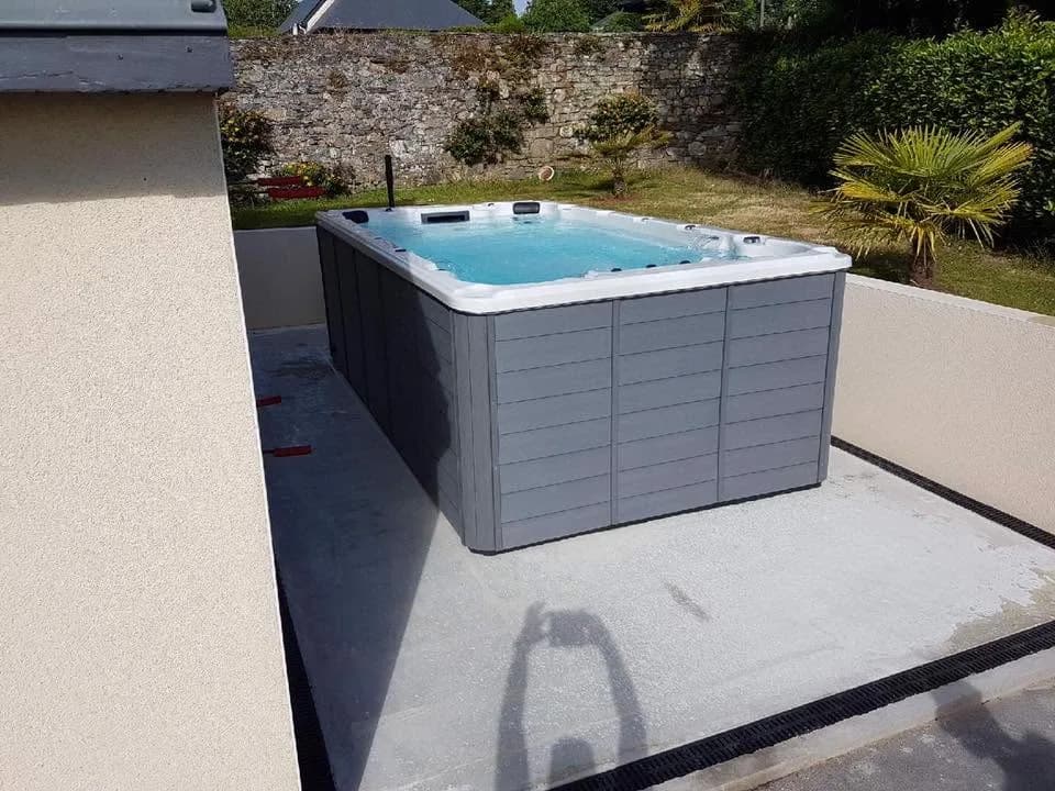 Installation d'un spa de nage Waterloo 421, sur une dalle grise en bordure de jardin