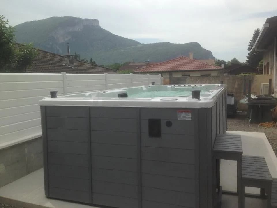 Installation d'un spa de nage Waterloo 501 Full option en Savoie, sur une dalle contre une palissade, face à la montagne
