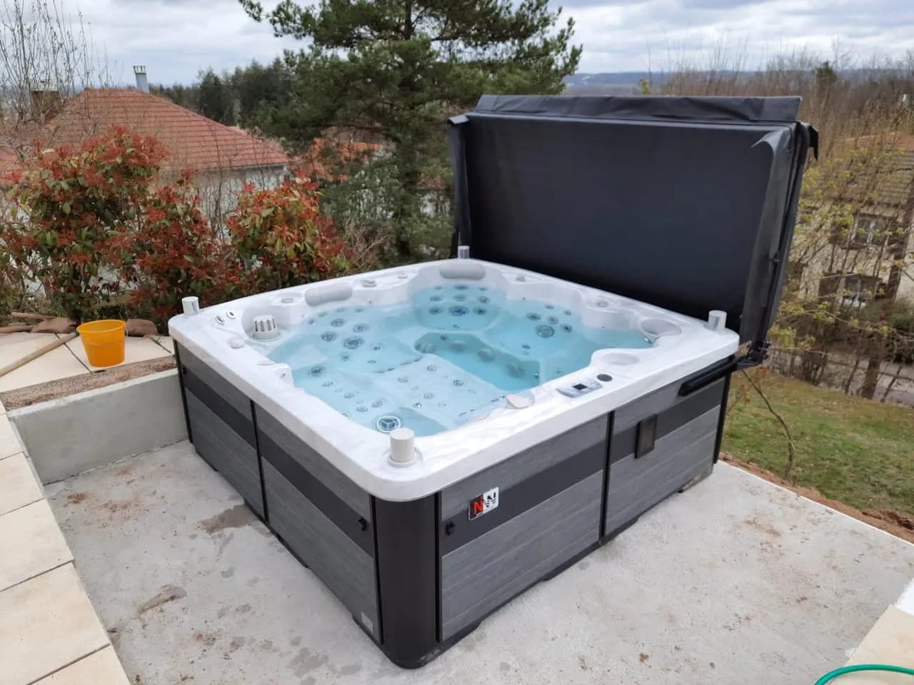 Installation d'un spa Hølen dans les Vosges, sur une dalle dans un jardin, lève-couverture