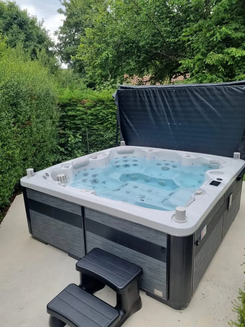 Installation d'un spa Hølen à Riedisheim, sur une dalle devant une haie, marchepied et lève-couverture
