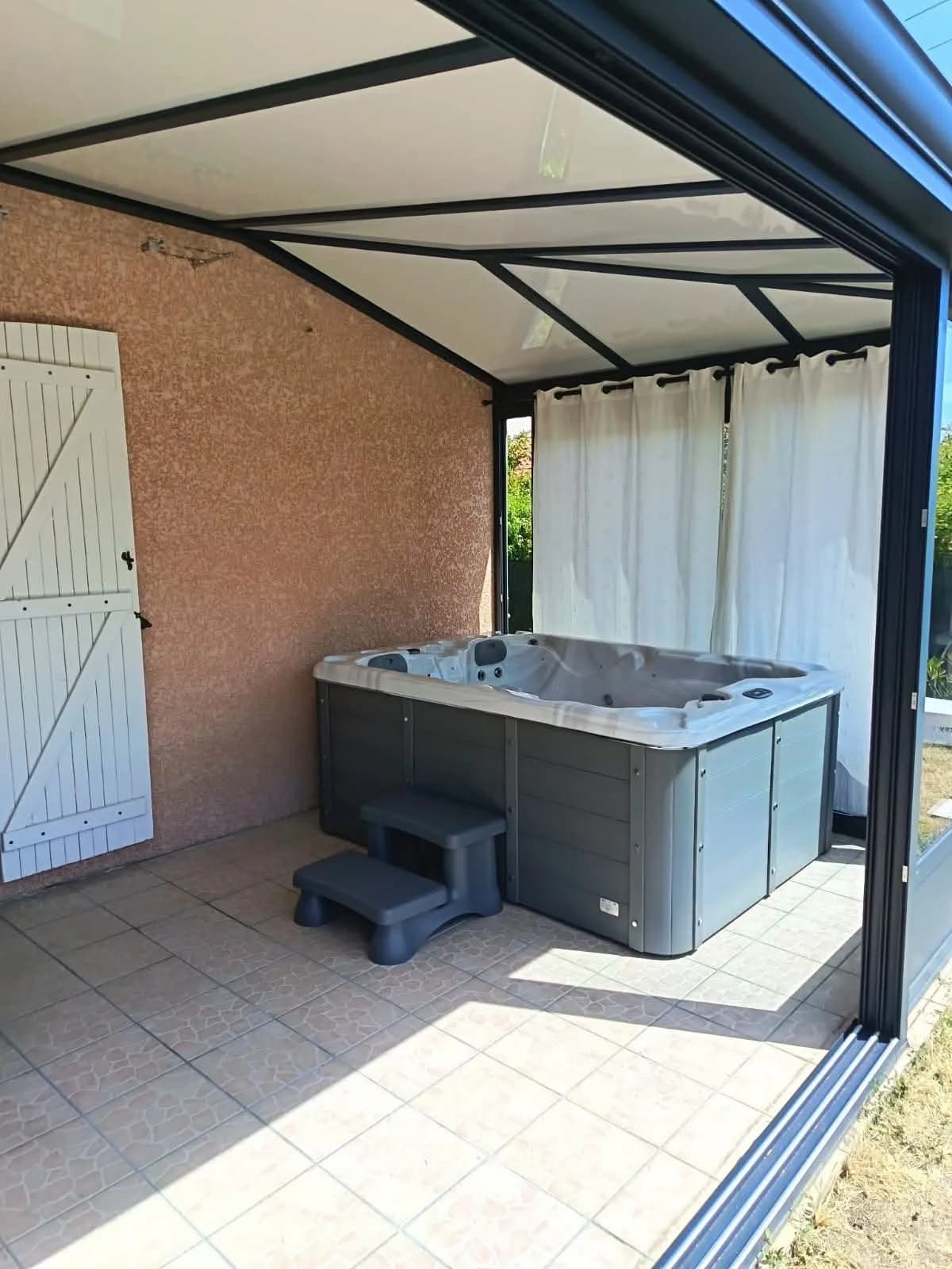 Installation d'un spa Montana à Aubière, sous une pergola à rideaux, terrasse carrelée