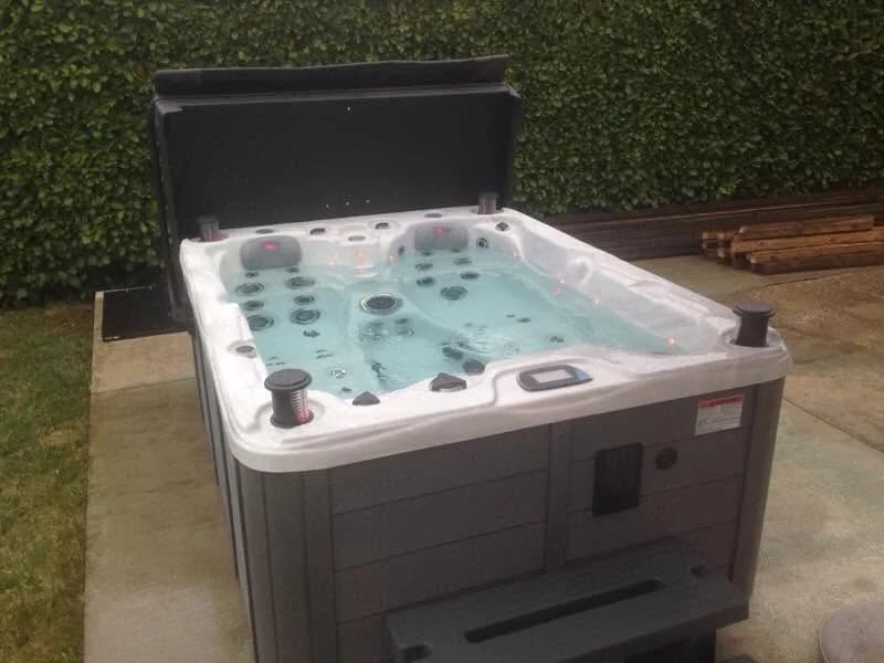 Installation d'un spa Montana Full option en Isère, sur une dalle devant une haie, marchepied