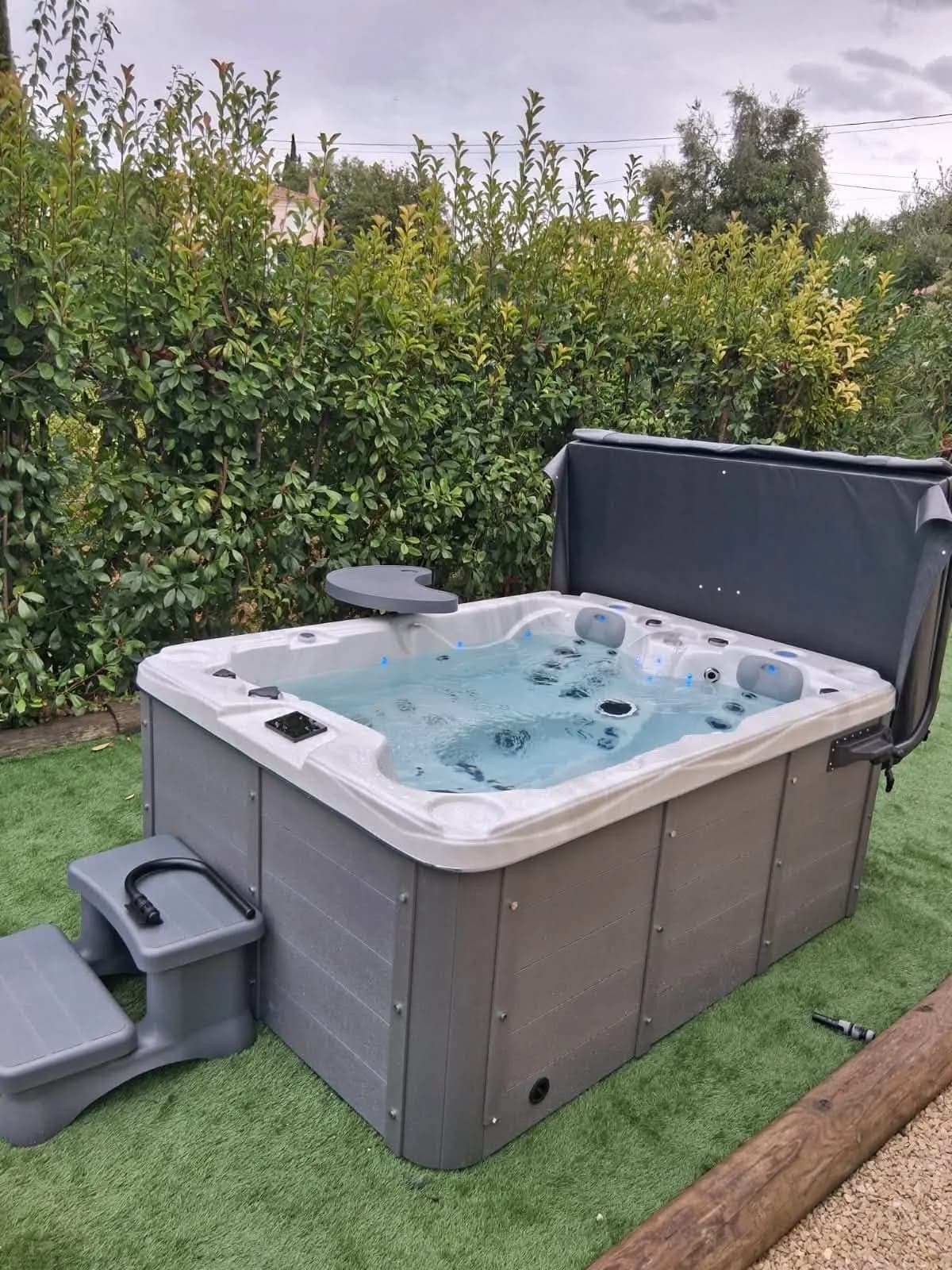 Installation d'un spa Montana à Saint-Jeannet, sur du gazon synthétique devant une haie, avec tablette et marchepied