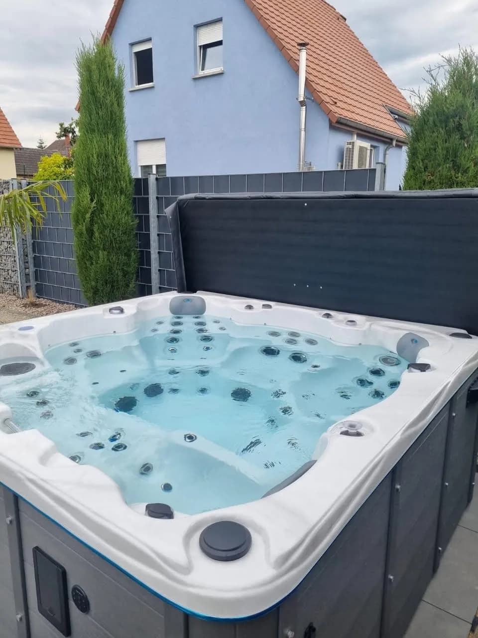 Installation d'un spa Montréal à Eischoffen, devant une palissade grise, couverture relevée