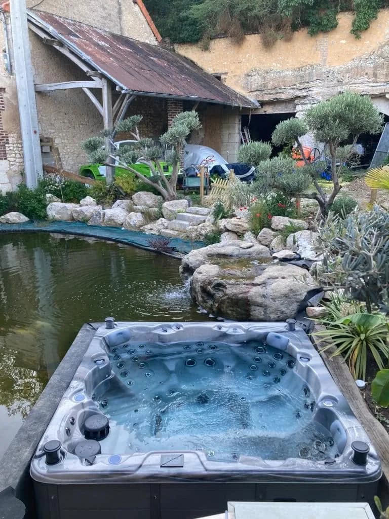 Installation d'un spa Montréal Full option à Naveil, au bord d'un bassin avec cascade