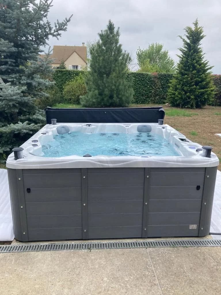 Installation d'un spa Montréal Full option à Neauphle-le-Château, en bordure de jardin devant des conifères