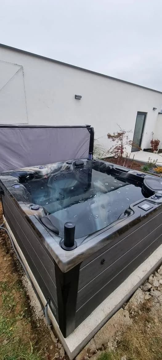 Installation d'un spa Onyx Full option à Aspach-le-Haut, contre un bâtiment, couverture relevée
