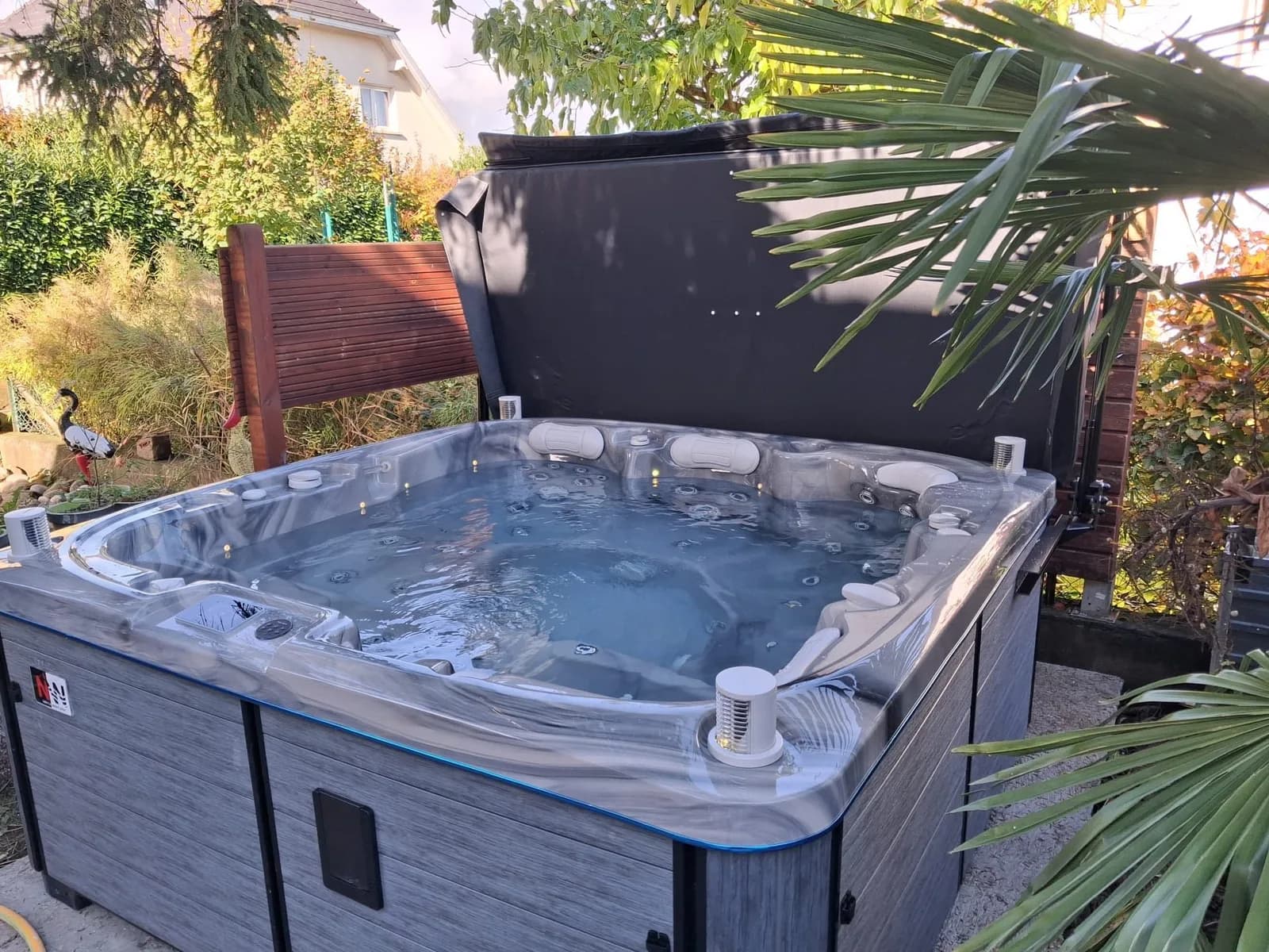 Installation d'un spa Øppland à Village-Neuf, dans un jardin de palmiers, contre un brise-vue en bois