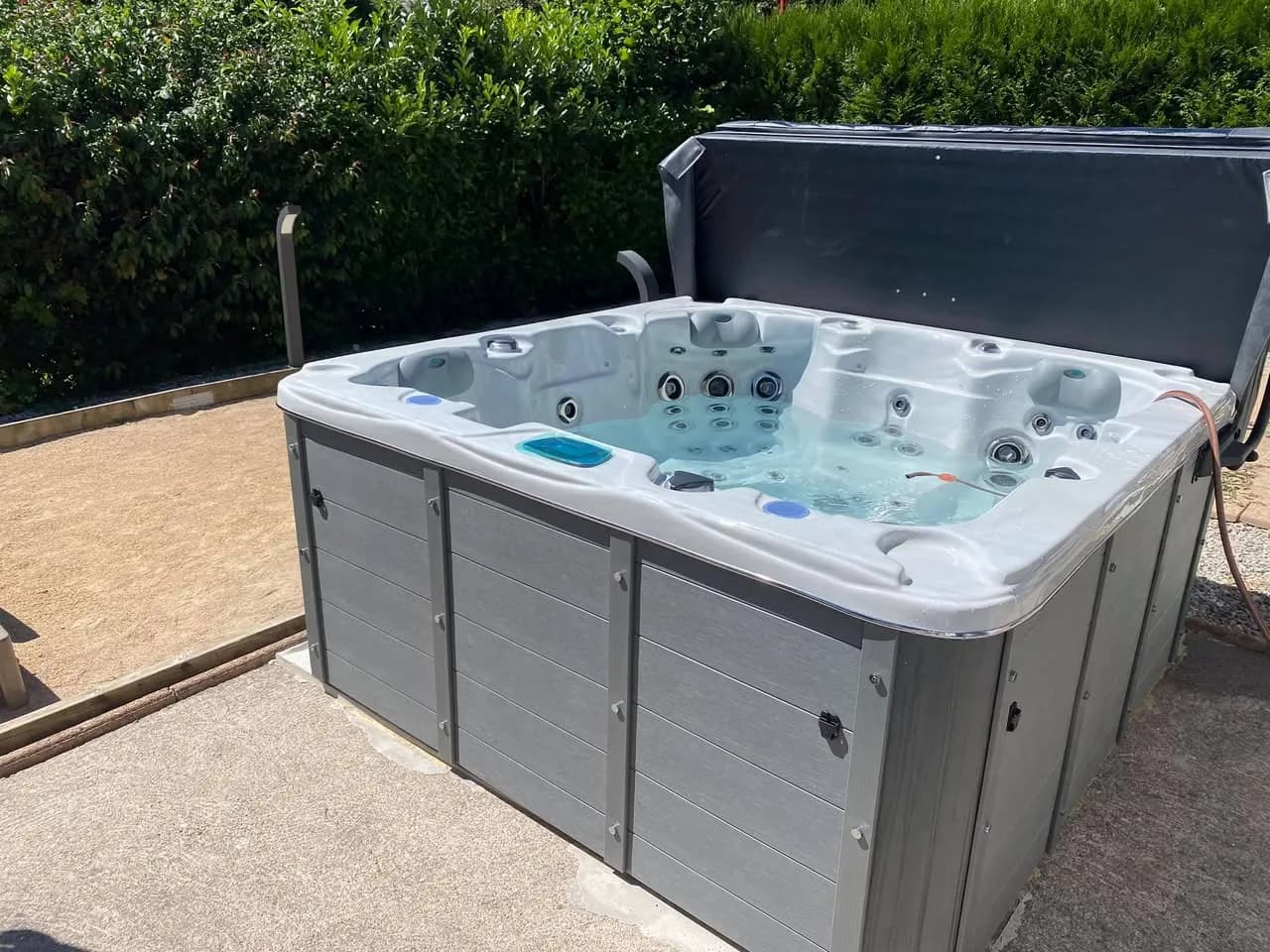 Installation d'un spa Ottawa à Novillard, sur une cour pavée, avec lève-couverture