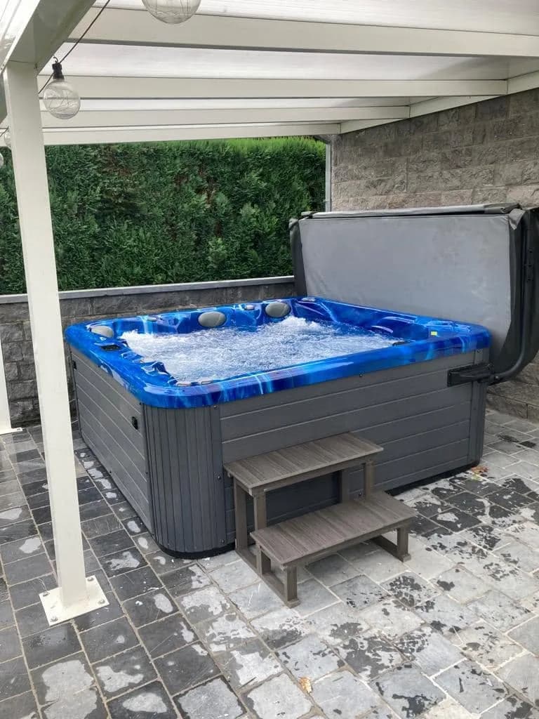 Installation d'un spa Poséidon à Juprelle, sous une pergola blanche, cuve bleue marbrée
