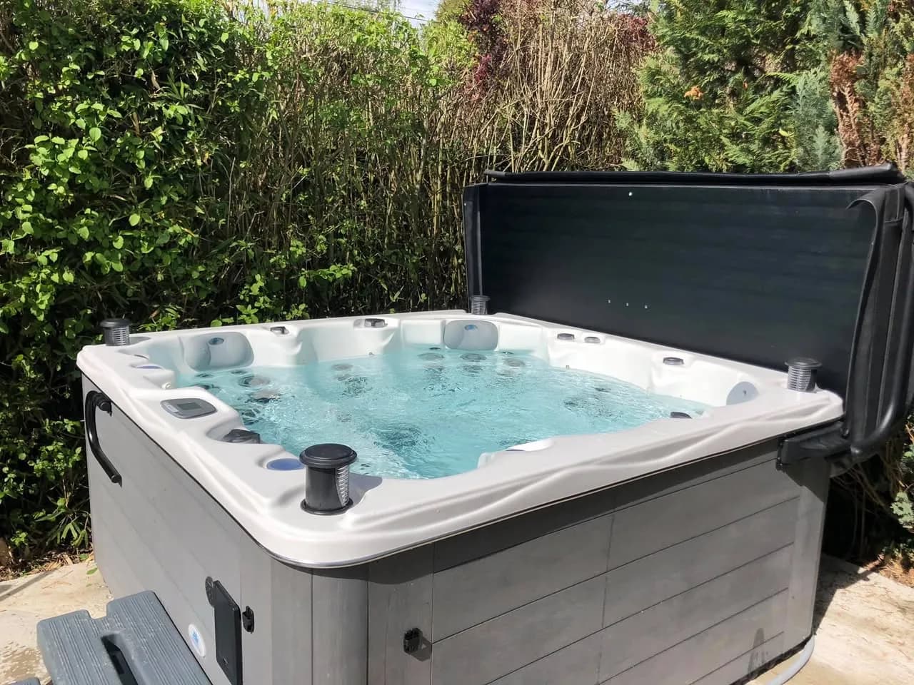 Installation d'un spa Québec à Mulhouse, devant une haie, couverture relevée