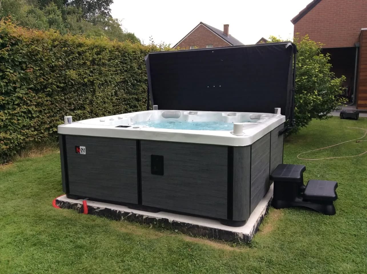 Installation d'un spa Sølveijg Full option en Belgique, sur la pelouse d'un jardin bordé de haies