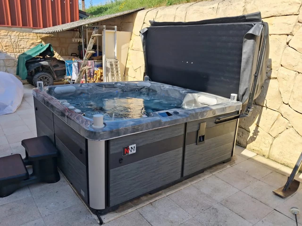 Installation d'un spa Sølveijg Full option à Illfurth, sur une terrasse dallée devant un mur en pierre