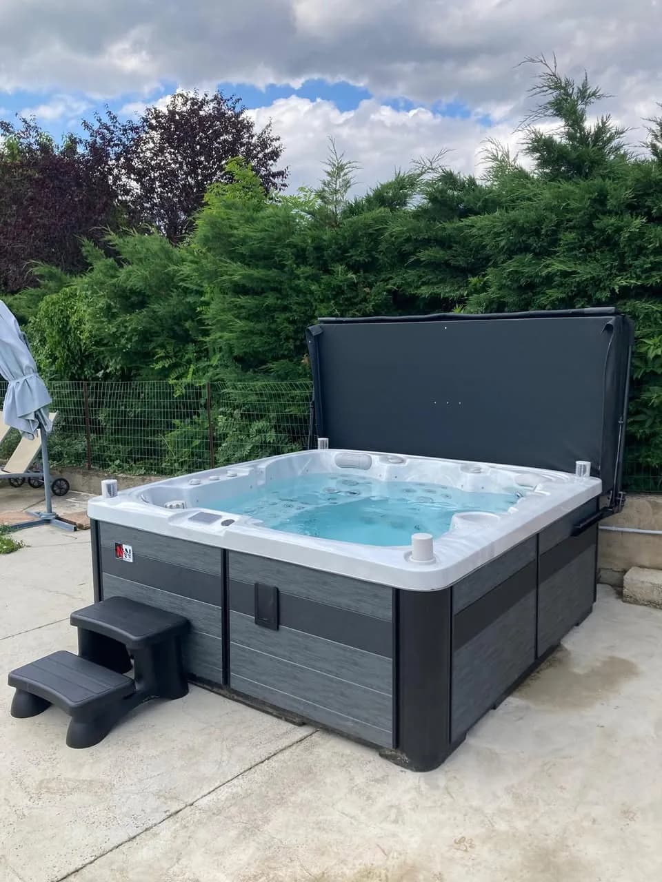 Installation d'un spa Sølveijg Full option à Solaize, sur une dalle devant une haie