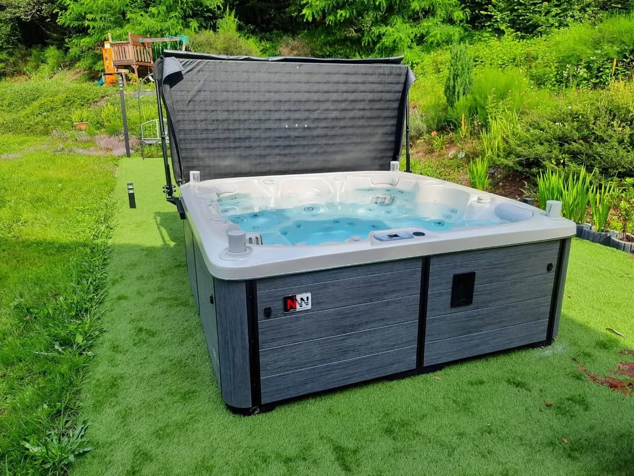 Installation d'un spa Søvik Full option à Belonchamp, sur un gazon synthétique, lève-couverture