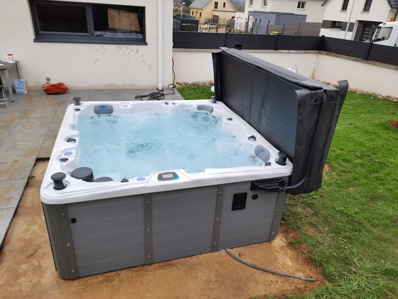 Installation d'un spa Sydney à Bessoncourt, sur une dalle au bord d'une pelouse, lève-couverture