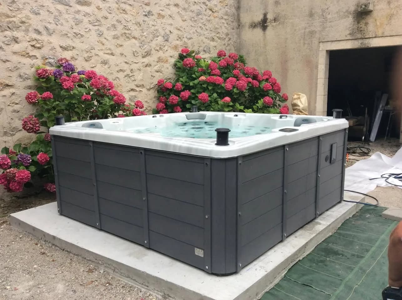 Installation d'un spa Sydney Full option à Cahors, au pied d'un mur de pierre, entre des hortensias
