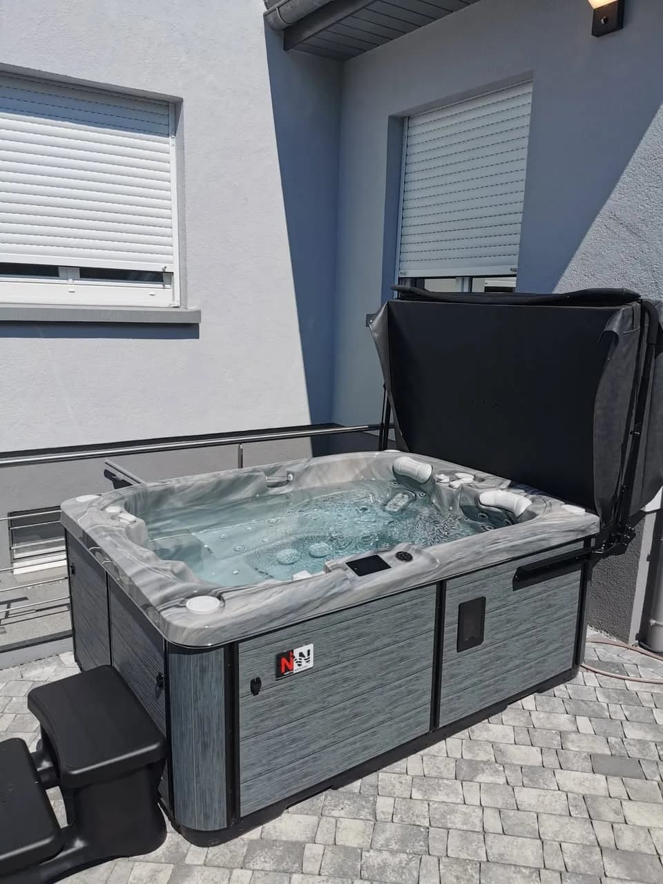 Installation d'un spa Tønsberg à Altkirch, sur une terrasse pavée contre la maison, lève-couverture