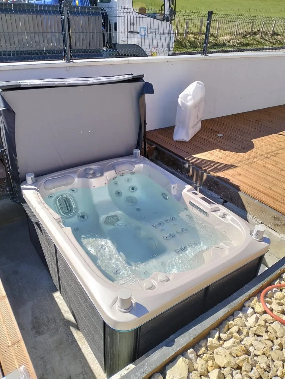 Installation d'un spa Tønsberg à Dommartin, sur une terrasse en bois contre un mur blanc