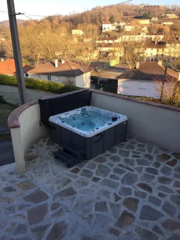 Installation d'un spa Toronto à Cransac, sur une terrasse en dallage de pierre, vue sur le village