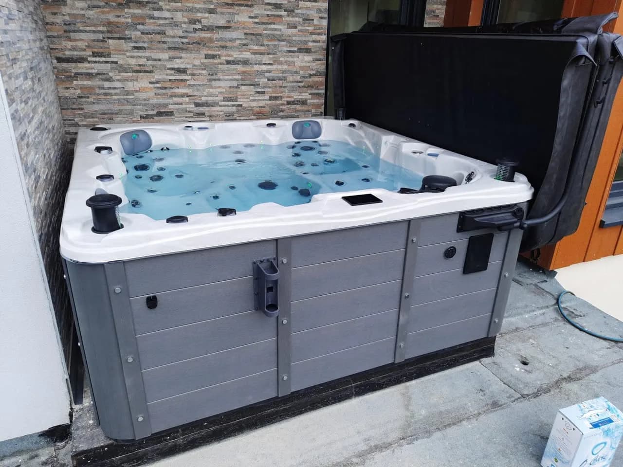 Installation d'un spa Toronto Full option à Illzach, contre un mur en parement de pierre, lève-couverture