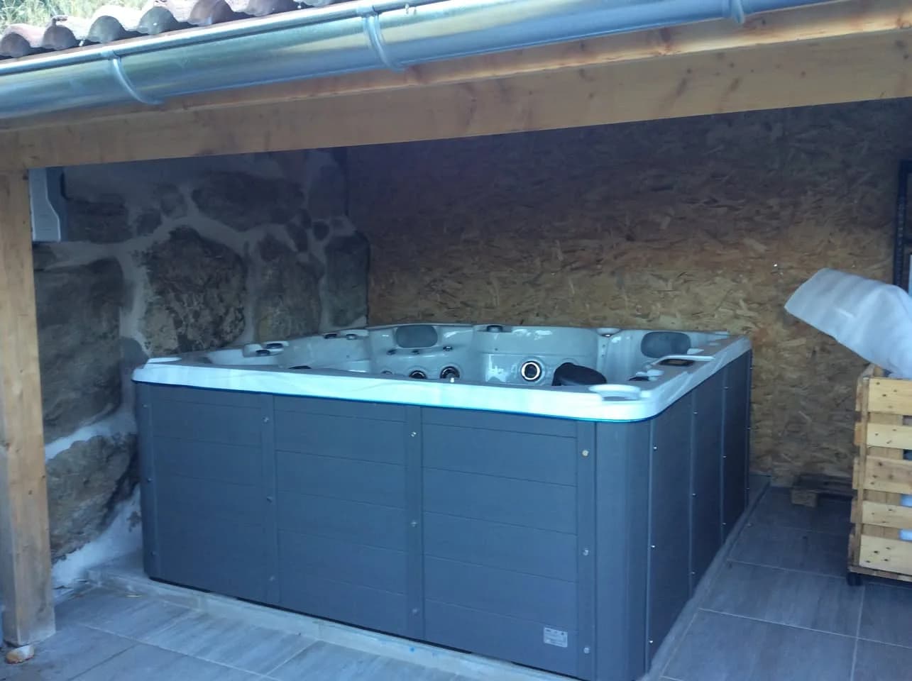 Installation d'un spa Vancouver à Barcillonnette, sous un abri en bois, contre un mur de pierre