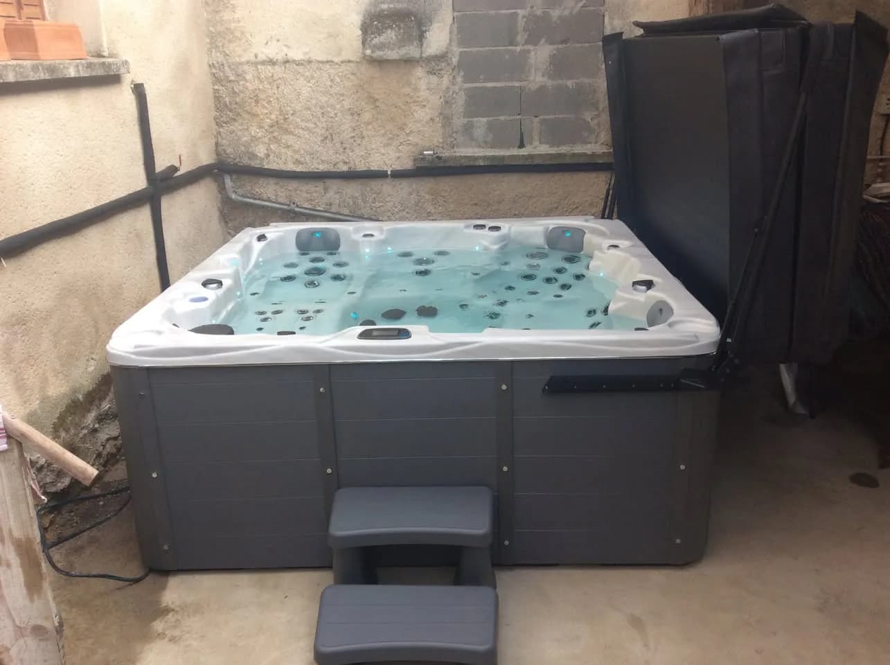 Installation d'un spa Vancouver à Châlaines, contre un mur en pierre, marchepied