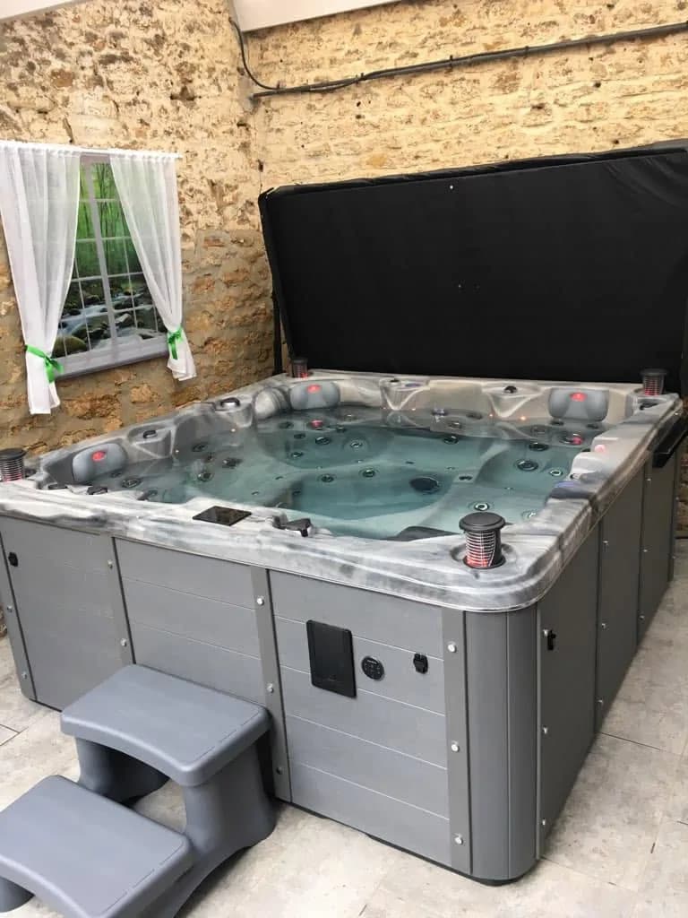 Installation d'un spa Vancouver Full option à Araucourt, sur une dalle contre un mur de pierre, marchepied