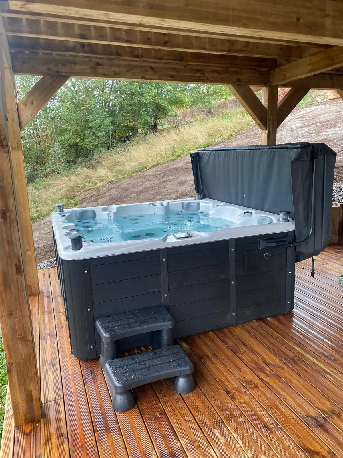 Installation d'un spa Vancouver Full option, tablier noir à Gérardmer, sous un abri en bois, sur une terrasse en bois
