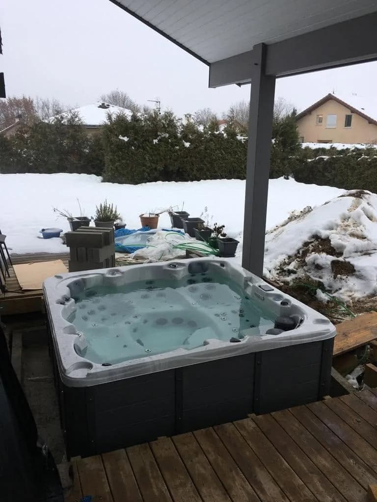 Installation d'un spa Vancouver à Saint-Genis-Pouilly, sous une pergola, terrasse en bois enneigée