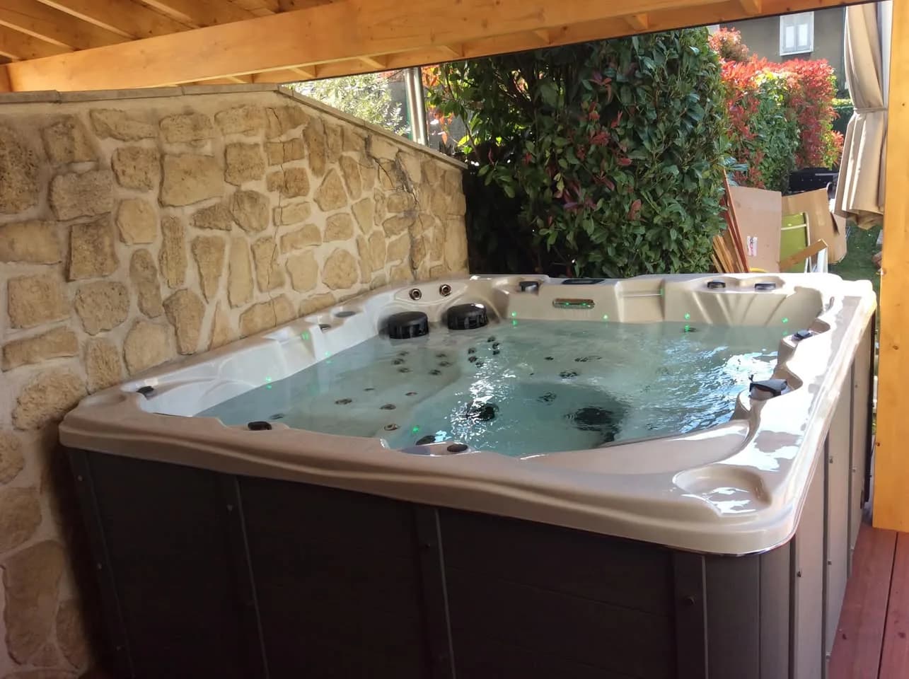 Installation d'un spa Vancouver à Saint-Georges, sous une pergola en bois, devant un mur en pierre