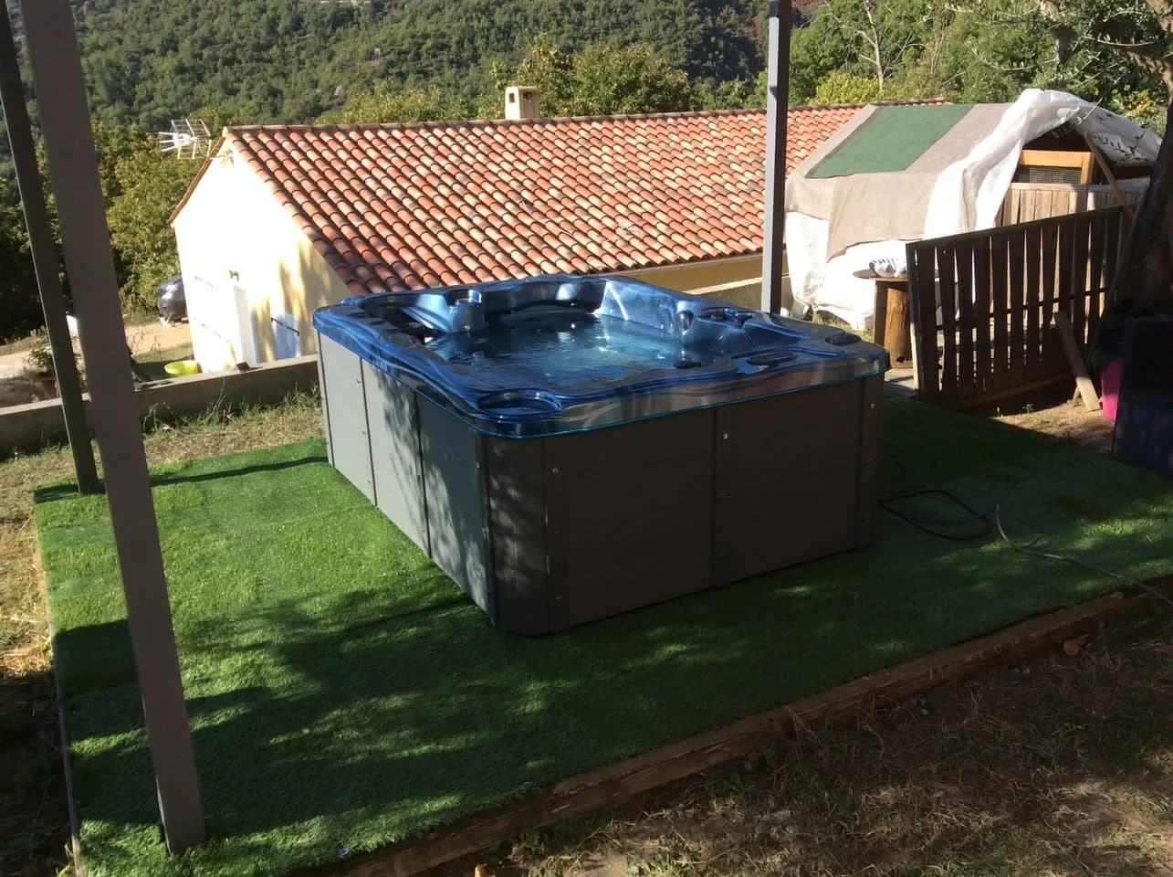Installation d'un spa Victoria Duel à Contes, sur un gazon synthétique sous une pergola, vue sur les collines