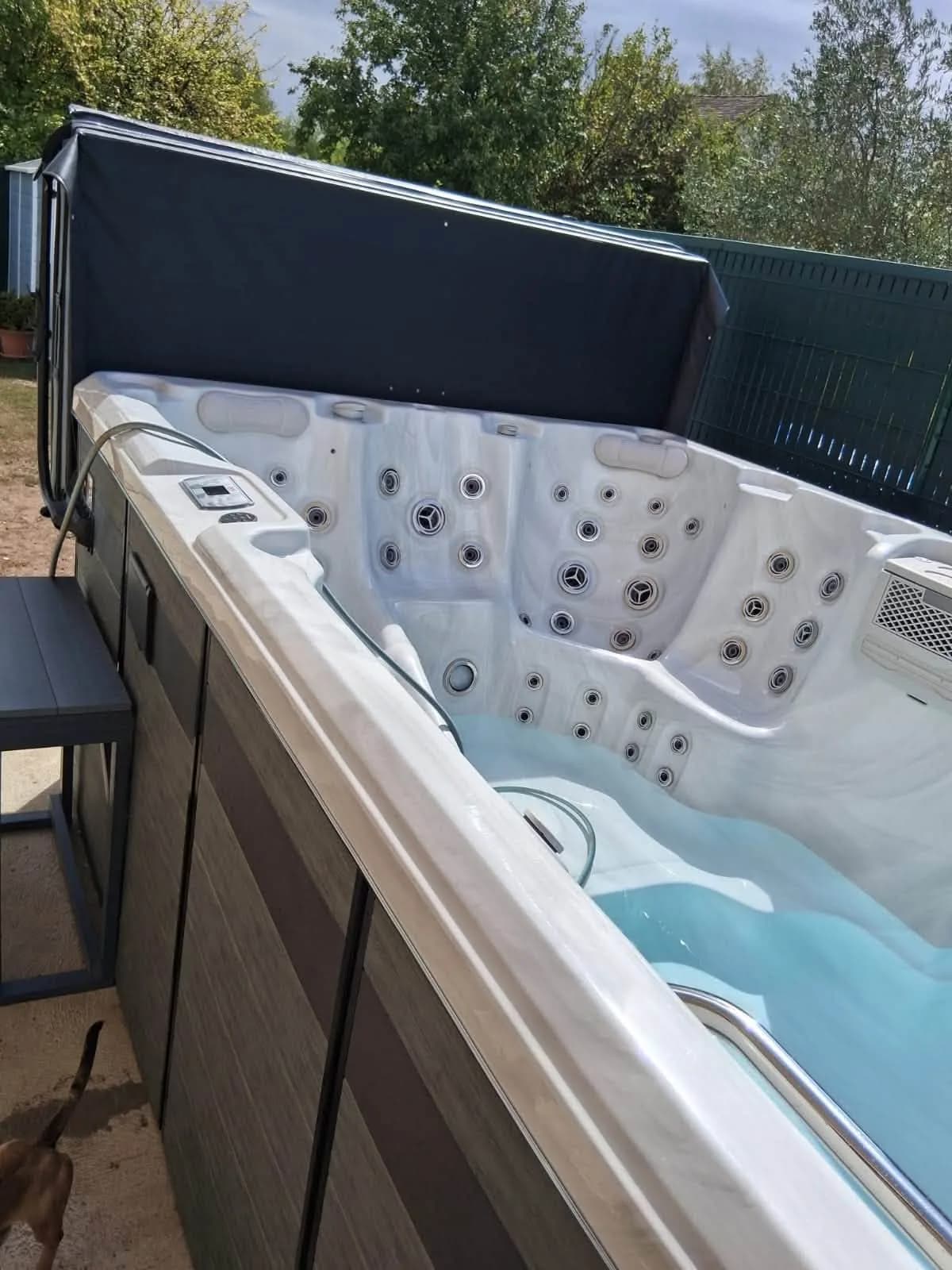 Spa de nage Oxford installé dans un jardin, bâche relevée sur toute sa longueur